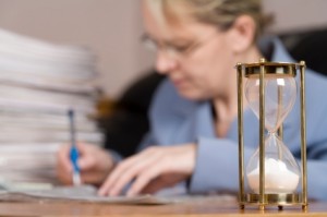 A woman doing taxes and expired hourglass in the foreground.